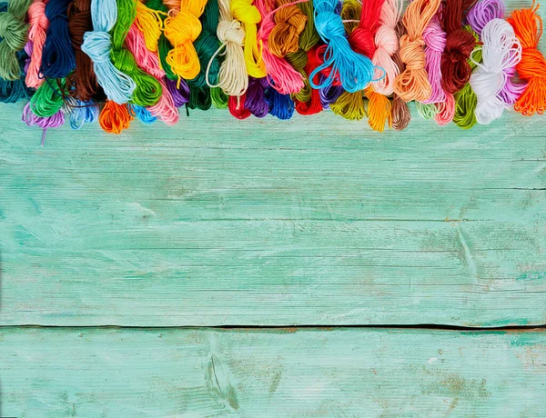 Ahşap turkuaz arka planda nakış işlemek için çok renkli iplikler.