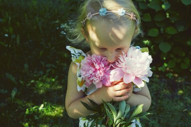 Yazlık elbiseli şirin küçük kız elinde şakayık demeti tutuyor.