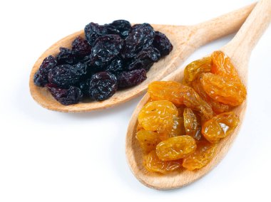 Beyaz arka planda izole edilmiş tahta kaşıkta altın ve siyah üzümler.