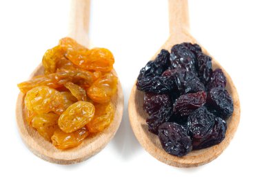 Beyaz arka planda izole edilmiş tahta kaşıkta altın ve siyah üzümler.