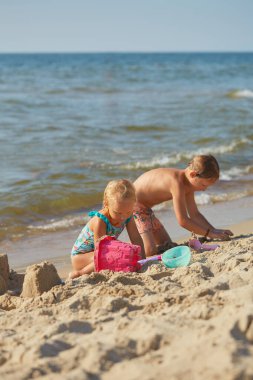 Çocuklar kumsalda oynuyor, kumdan kaleler yapıyorlar.