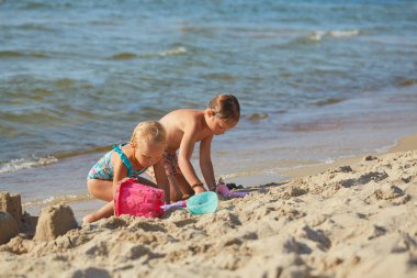 Çocuklar kumsalda oynuyor, kumdan kaleler yapıyorlar.