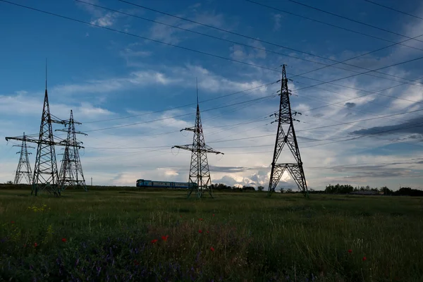 Train on the horizon with power lines in the foreground.Power lines and sky with clouds.Wires over the fields.Powerful lines of electric gears.Field and aerial lines, silhouettes at dusk.