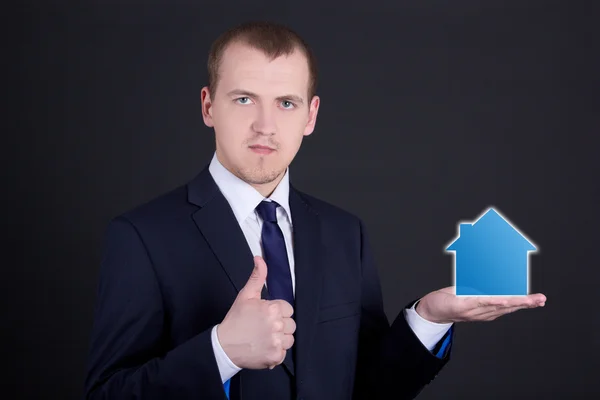 Empresario sosteniendo una casa pequeña en su mano y los pulgares —  Fotos de Stock