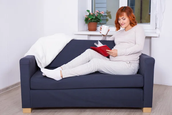 Feliz mujer embarazada bebiendo té y leyendo libros en casa — Foto de Stock