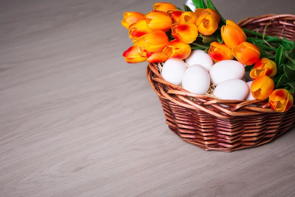 Easter eggs and tulips in basket on wooden table — Stock Photo, Image
