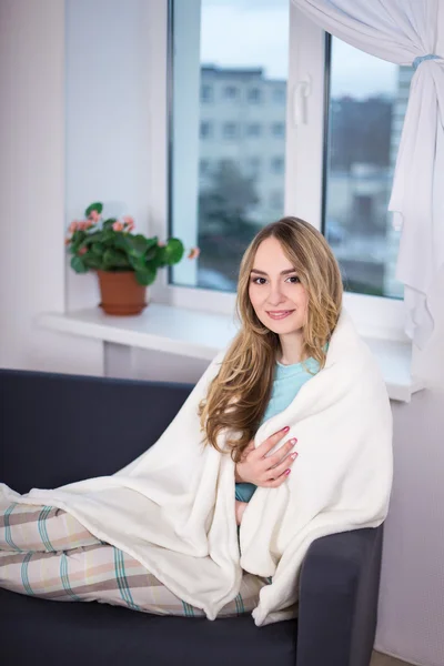 Young woman in pajamas wrapped in blanket sitting in bedroom — Stock Photo, Image