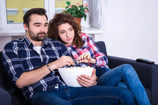 Jovem casal assistindo filme na tv e comendo pipoca em casa — Fotografia de Stock