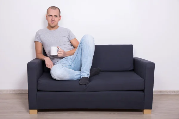 Przystojny mężczyzna siedzi na kanapie i oglądać tv z filiżanką herbaty — Zdjęcie stockowe
