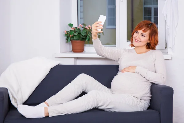 Jovem mulher grávida tomando selfie foto com telefone inteligente em hom — Fotografia de Stock