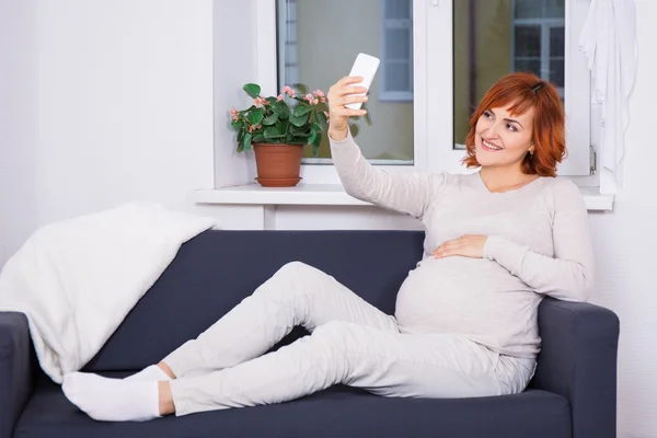 Junge schwangere Frau unter Selfie Foto mit Smartphone bei hom — Stockfoto