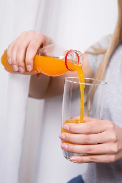 Frau Orangensaft aus der Flasche in das Glas gießen — Stockfoto