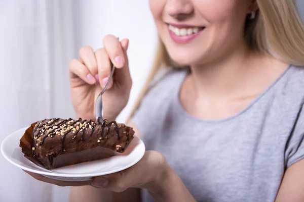 Młoda kobieta uśmiechający się jedzenia czekoladowe ciasto w domu — Zdjęcie stockowe