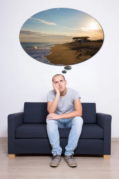 Přemýšlivý muž sedí na pohovce a snít o dovolené — Stock fotografie