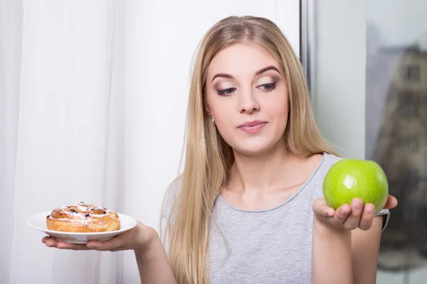 Diet concept - woman choosing behind pastry and green apple — Stock Photo, Image