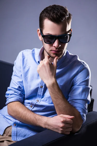 Portré, szép ember ül a kanapén, és gondolom napszemüveg — Stock Fotó
