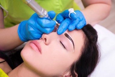 close up of cosmetologist applying permanent make up on eyebrows clipart