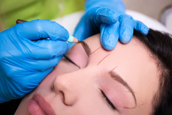 cosmetician preparing young woman for permanent eyebrow make up