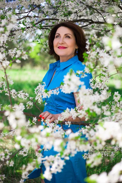 Middle aged woman with blooming cherry tree in garden — Stock Photo, Image