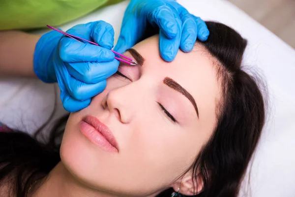 Woman getting tweezing eyebrow by beautician — Stock Photo, Image