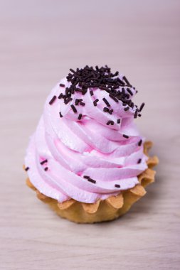 küp kek pembe krema ve çikolata yongaları üzerinde ahşap backgro ile