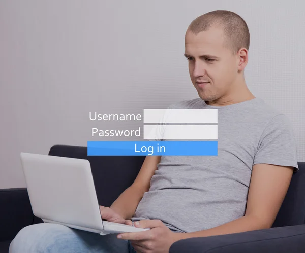 Young handsome man sitting on sofa with computer and registering — Stock Photo, Image