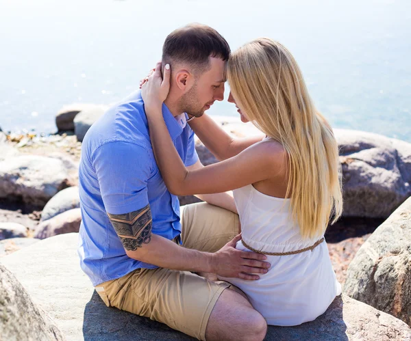 Lyckliga unga vackra paret sitter på stenig strand — Stockfoto