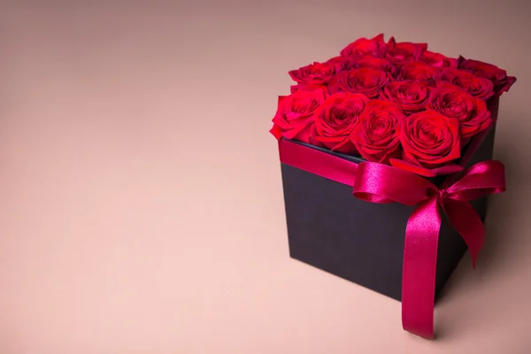 Black box with beautiful red rose flowers over beige background — Stock Photo, Image