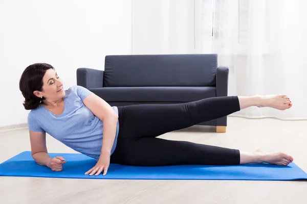 Slim mulher madura desportiva fazendo exercícios de alongamento no tapete de ioga — Fotografia de Stock
