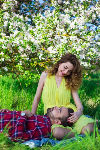Young beautiful couple sitting in blooming garden — Stock Photo, Image