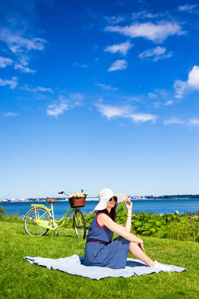 Genç kadın vintage bisiklet ile deniz kıyısında oturan şapkalı — Stok fotoğraf