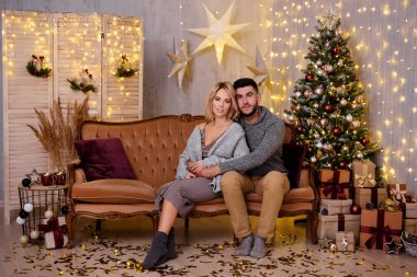 kış tatili ve ilişki konsepti - oturma odasında süslenmiş Noel ağacı, hediyeler ve ışıklar olan mutlu genç çift