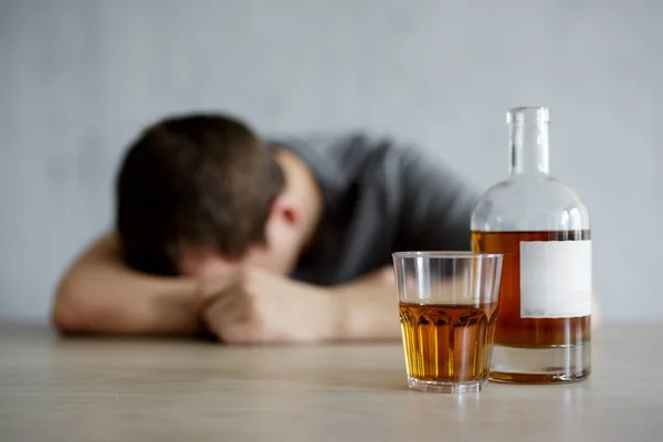 アルコール依存症とうつ病の概念 テーブルの上に横たわるウイスキーと酔って男のガラスとボトルのクローズアップ — ストック写真