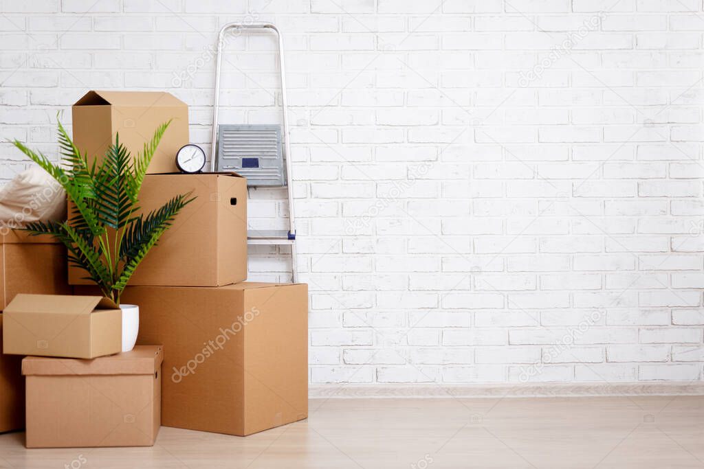 moving day concept - cardboard boxes, houseplants and other things over white brick wall background with copy space