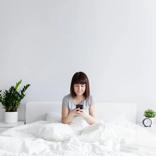 Glückliche Frau Sitzt Auf Dem Bett Und Nutzt Smartphone Hause — Stockfoto