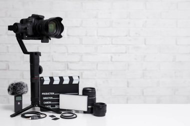 Video konsepti - 3 eksenli dengeleyici, lensler, mikrofon, öncü ışık, kleptik tahta ve diğer video ekipmanları üzerine beyaz tuğla duvar arkaplanı ve fotokopi alanı üzerine modern DSR kamera