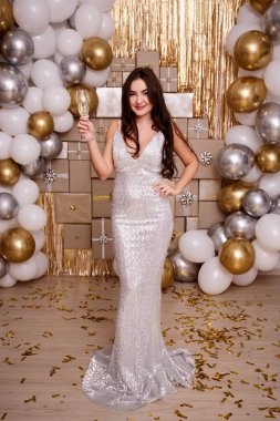 Doğum günü, Noel ya da yeni yıl kutlaması konsepti. Mutlu, gümüş elbiseli, şenlikli bir kadın hediye kutuları ve hava balonları üzerine poz veriyor.