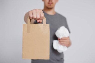 Konsepti küçült, yeniden kullan ve geri dönüştür - plastik torba ve kahverengi geri dönüşümlü kağıt torba erkek elinde gri arka plan üzerinde