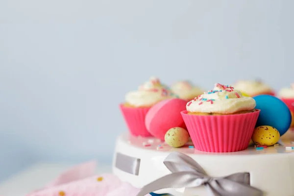 Easter sweets and decorations - close up of cream cupcakes and colorful painted eggs over white wall with copy space