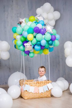 Çocukluk, hayaller ve yaratıcılık konsepti. Stüdyoda renkli hava balonu sepetinde oturan gülümseyen küçük kız.