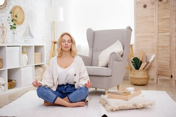 dreaming and relaxation concept - portrait of cute blond woman sitting in yoga pose in living room