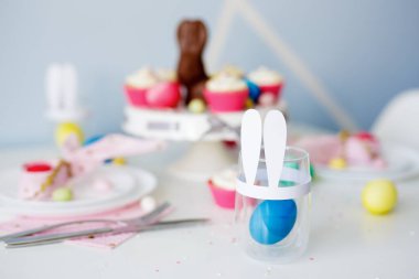 Kapkeklerle süslü masa, renkli boyanmış yumurta ve tavşan kulaklı cam.