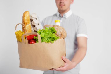 Teslimatçı, beyaz arka planda bir çanta dolusu ürün veriyor.