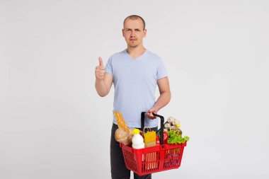 Alışveriş sepeti dolusu ürünü olan genç bir adamın portresi beyaz arka planda.