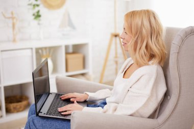 İnsanlar ve teknoloji konsepti - parlak oturma odasında dizüstü bilgisayar kullanan güzel bir kadının yan görüntüsü