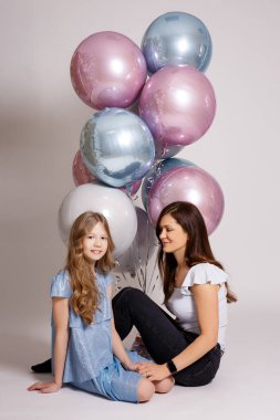 Beyaz arka planda oturan pastel renkli balonları olan anne ve kızı.