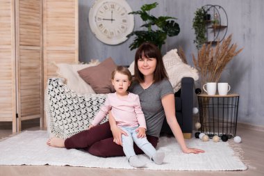 Oturma odasında oturan genç bir kadın ve küçük tatlı kızının portresi.