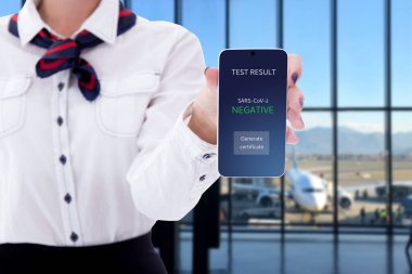 Coronavirus, aşılama ve seyahat konsepti - Coronavirus testli akıllı telefon havaalanında hosteslerin ellerinde ekrana yansıyor