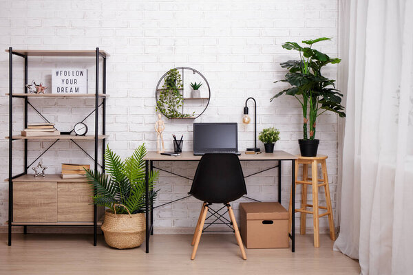 Workplace with table, chair, rack and plants over brick wall