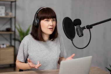 Kadın ev ofisinde mikrofon ve dizüstü bilgisayar kullanarak ses yayını yapıyor.